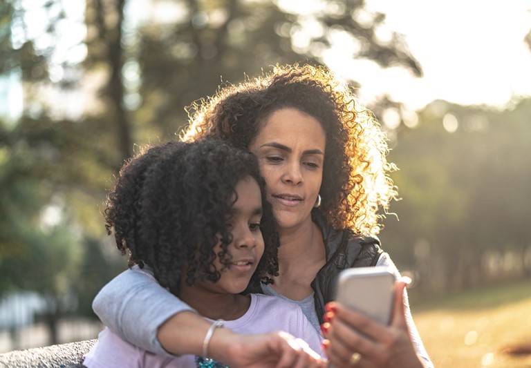 African American mom looking at cell phone with daughter.